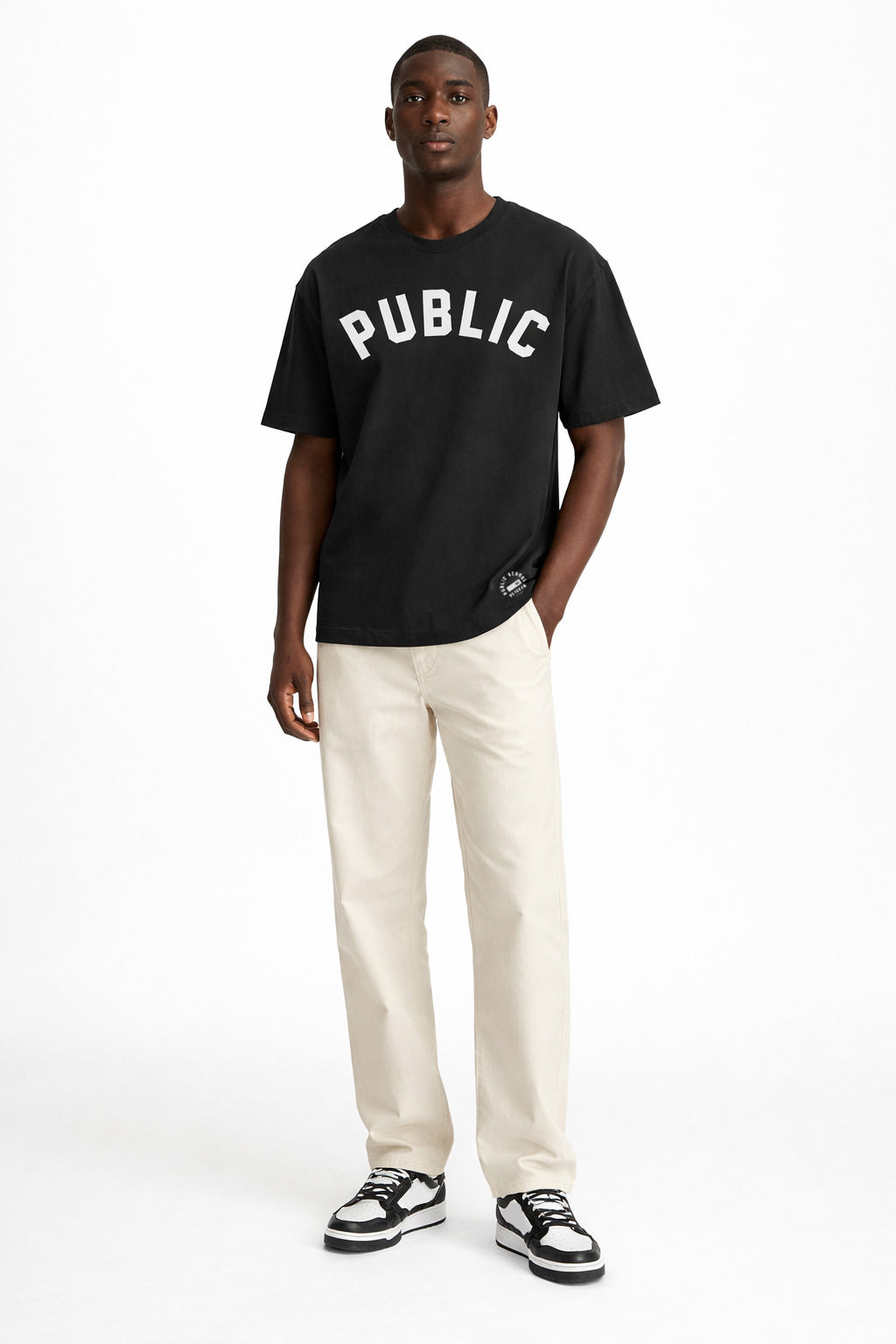 Man wearing a black t-shirt with 'PUBLIC' text and white pants on a white background